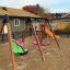 Xích đu Double Seat swing với khung gỗ và ghế nhựa màu xanh và hồng trên sân chơi cát.